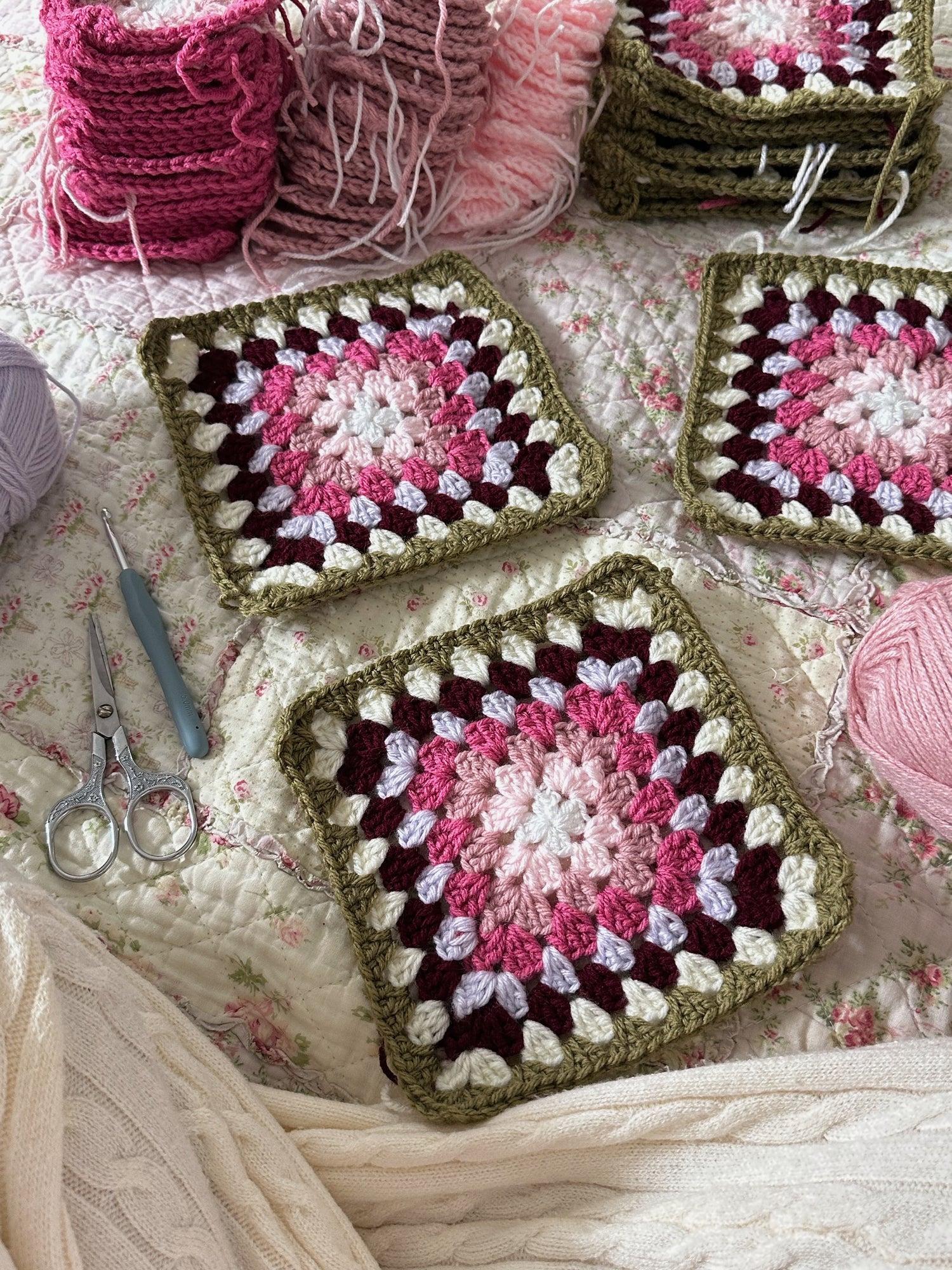 Crocheted granny squares with yarn and scissors on a floral fabric background