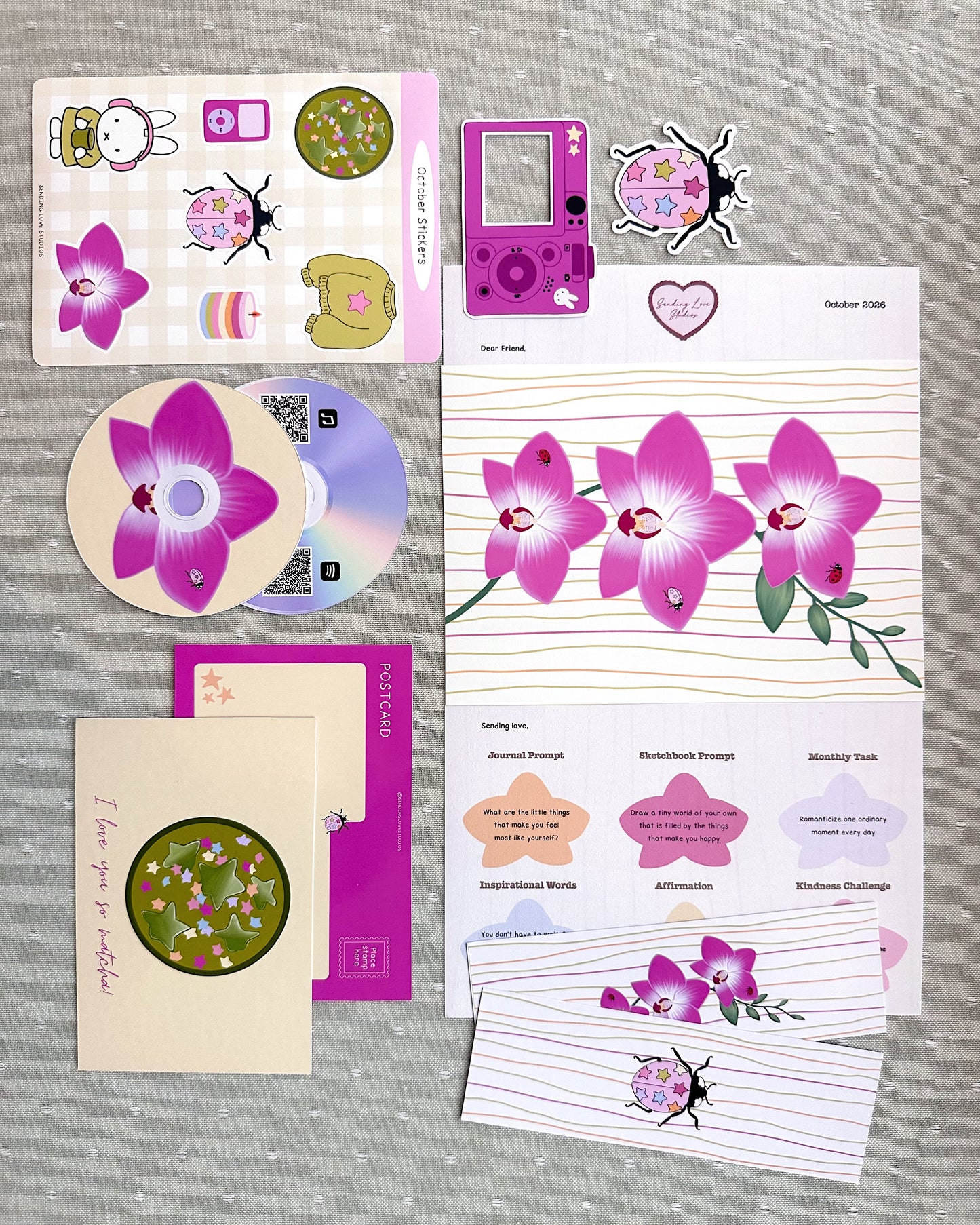 a pink orchid art print, ladybug and digital camera vinyl stickers, sticker sheet, matcha postcard, ladybug and orchid double sided bookmark, CD playlist print, and letter all printed and laid out on a table 